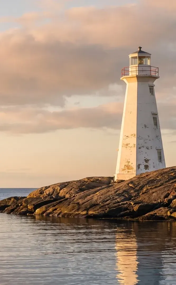 A lighthouse on a rocky headland at sunset over calm water