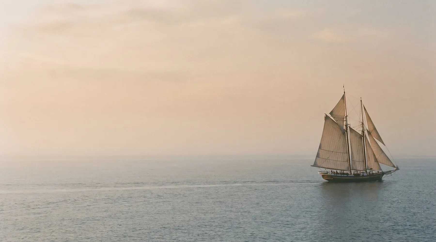 A classic sailing vessel under full sail crossing open water at sunset